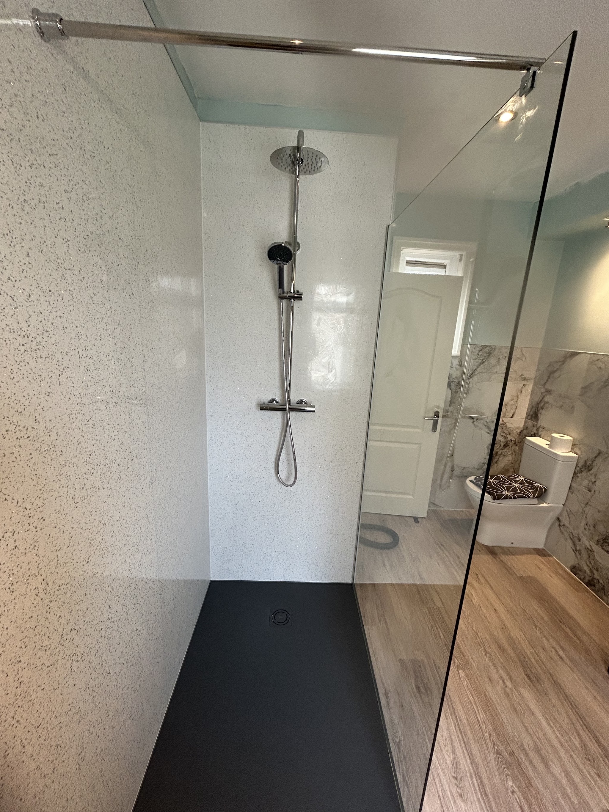 A completed shower enclosure with pale wall panels and a black shower tray